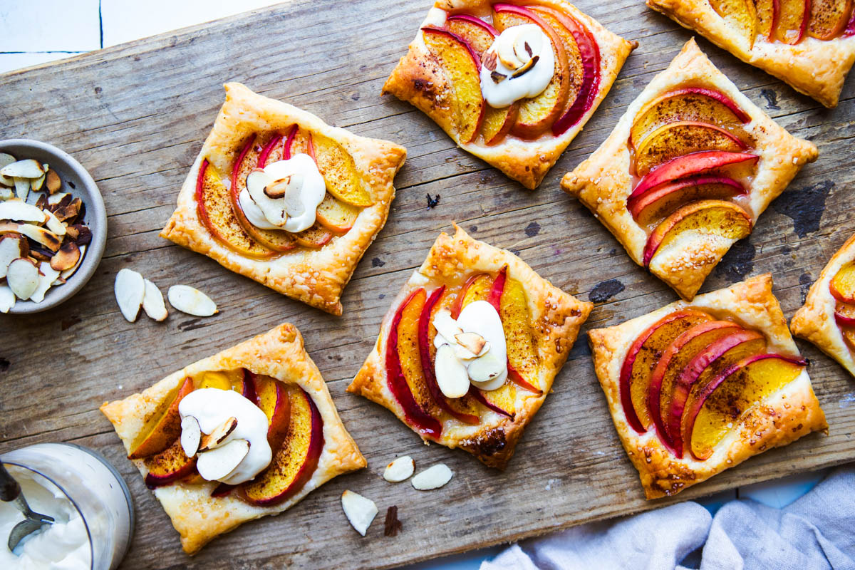 peach puff pastry tarts on a wood board with a whipped cream cheese topping