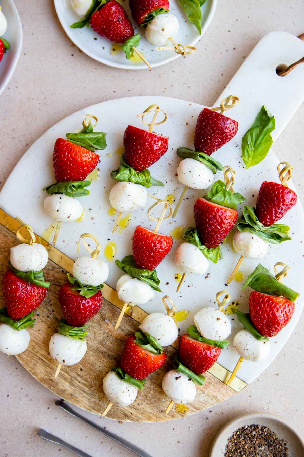 mini caprese skewers made with fresh strawberries and served on a marble platter and garnished with olive oil drizzle and black pepper