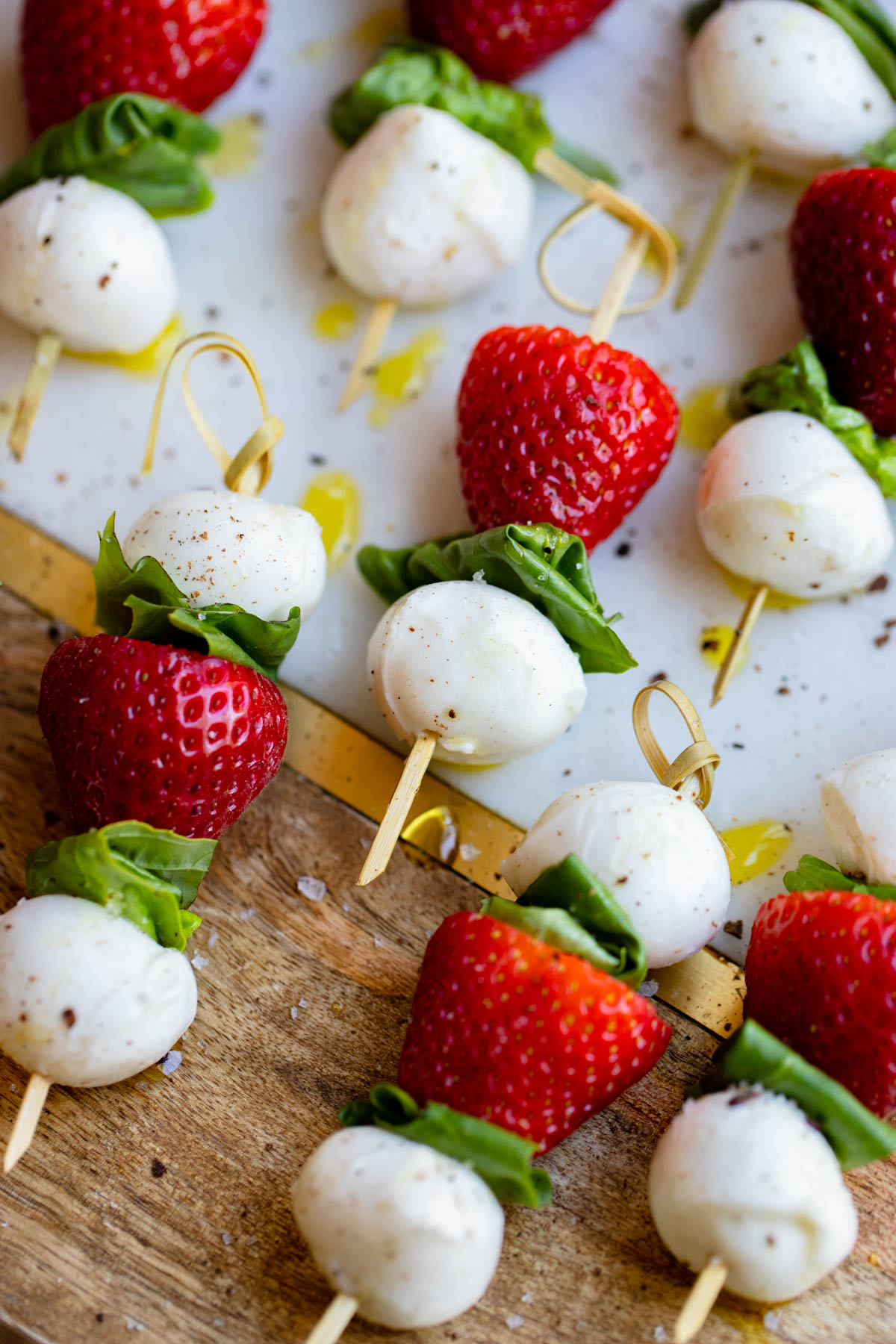 caprese mini skewers made with strawberries and basil on a wood board