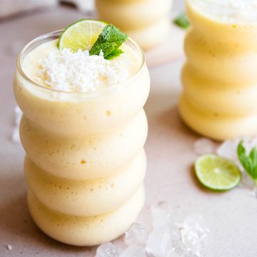 mango protein smoothie garnished with lime and coconut and mint leaves in a glass