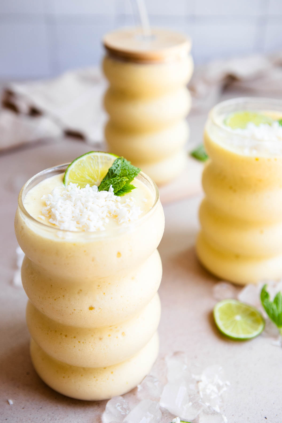 3 wavy glasses filled with a mango protein smoothie and garnished with lime and shredded coconut