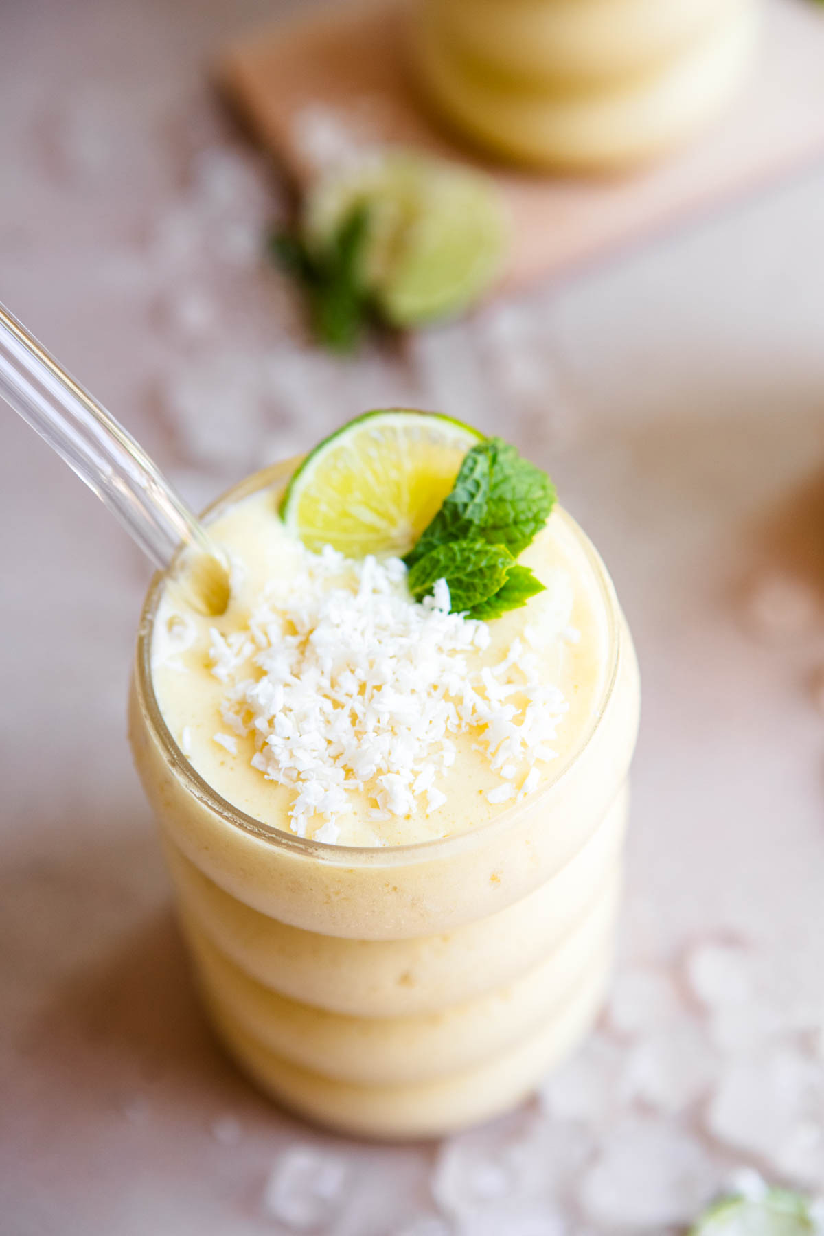 mango protein smoothie garnished with lime and mint in a cute glass with glass straw