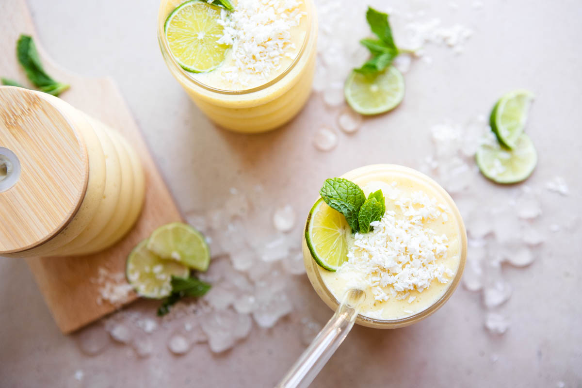 3 smoothie glasses filled with a protein smoothie made with mango and green apple and garnished with mint leaves and lime wedges