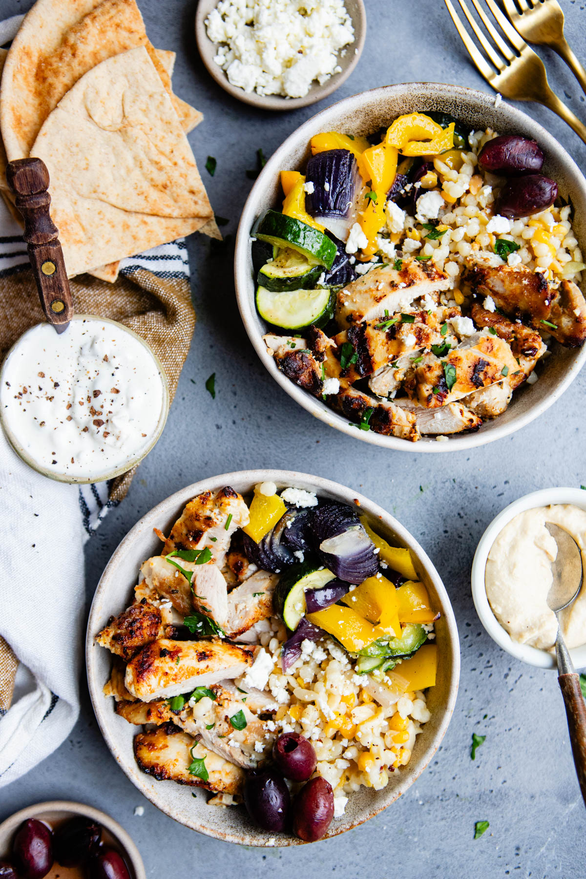 Mediterranean chicken bowls in ceramic bowls and topped with feta and garlic yogurt sauce