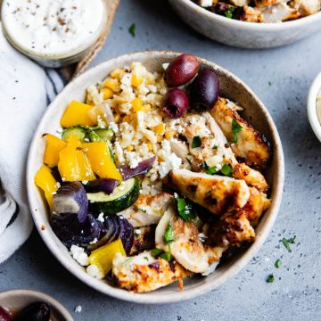 beige bowl filled with couscous and roasted vegetables and grilled Mediterranean chicken
