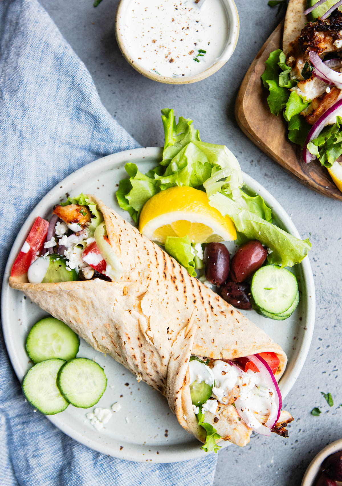 a plate with a Mediterranean chicken wrap and cucumber and olive garnishes