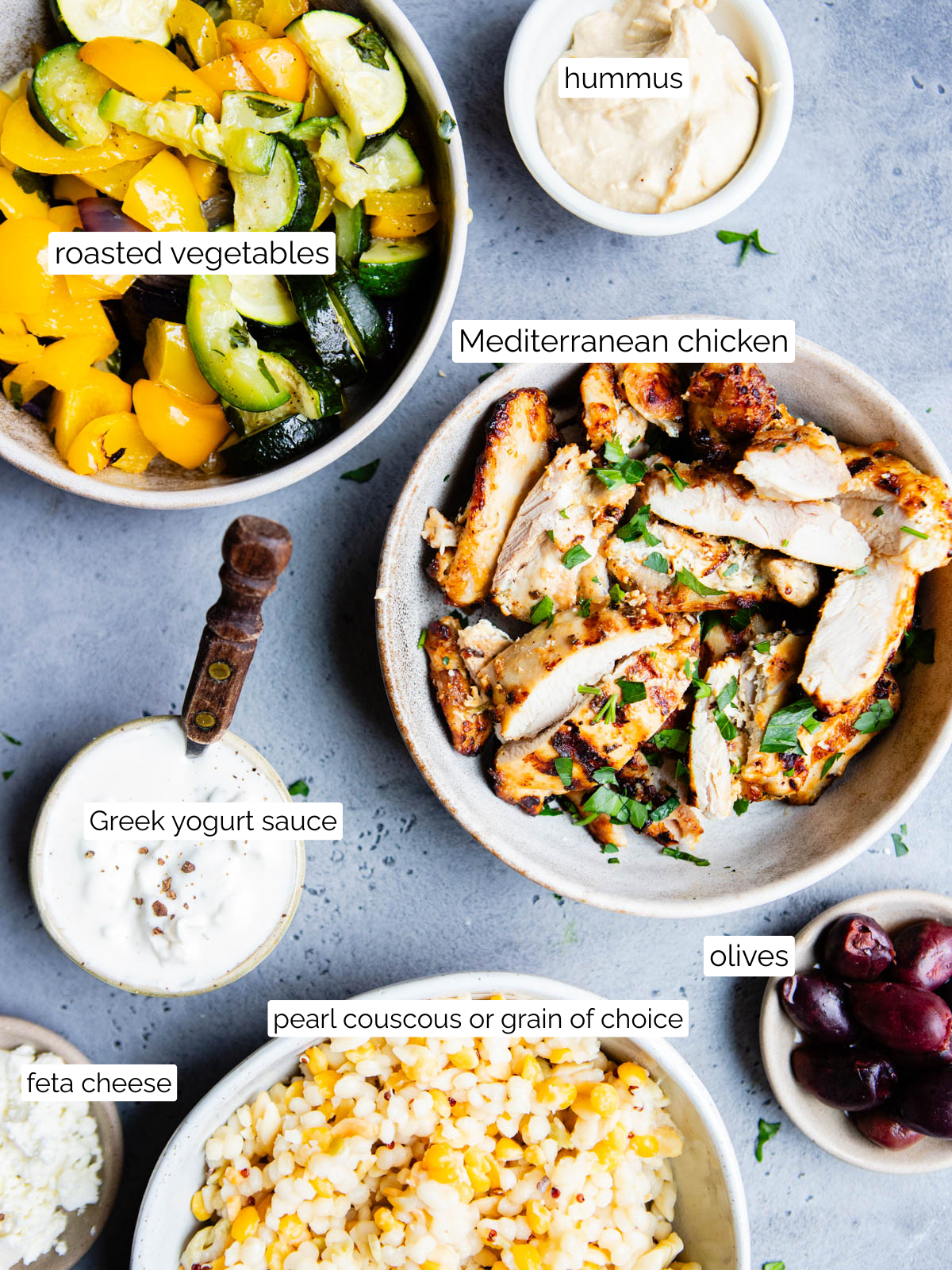 grilled chicken, cooked pearl couscous and roasted vegetables in bowls along with hummus, dip and olives 