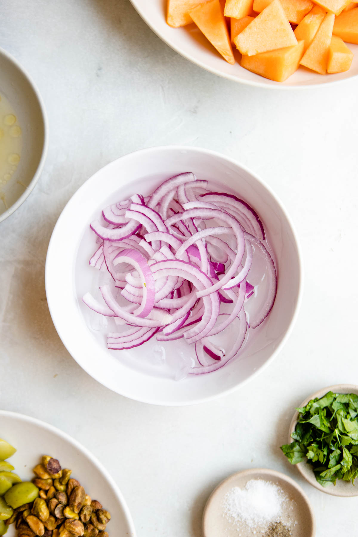 sliced red onions soaking in a bowl of ice water to remove their bitterness