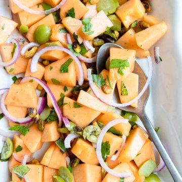 cantaloupe melon salad with pistachios and green olives on a white serving platter