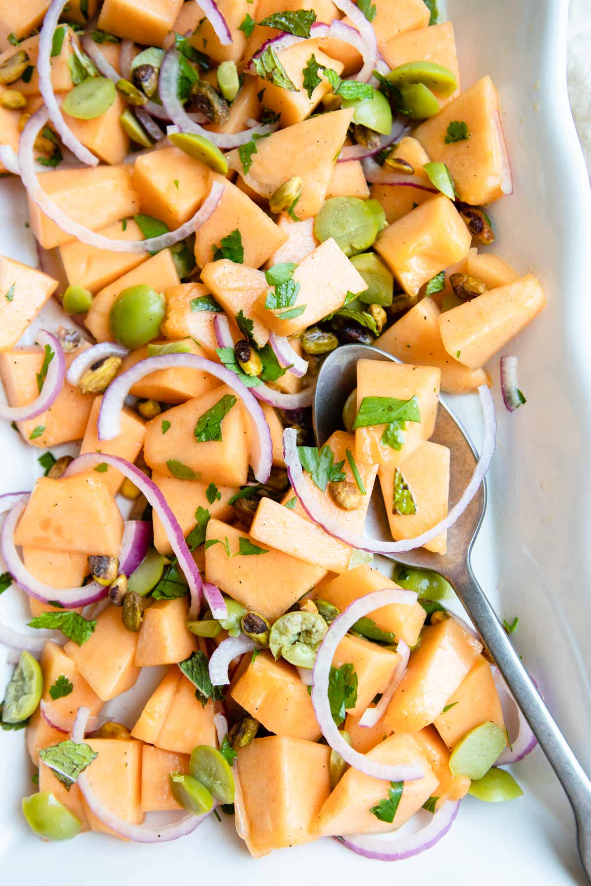 cantaloupe salad on a white platter with a large serving spoon