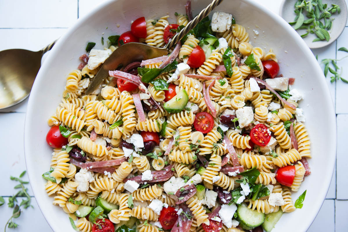 large white ceramic bowl filled with high protein pasta salad and garnished with feta cheese and fresh oregano 