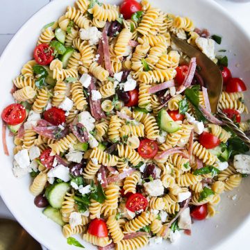 protein pasta salad with vegetables in a white ceramic bowl and bronze serving utensils