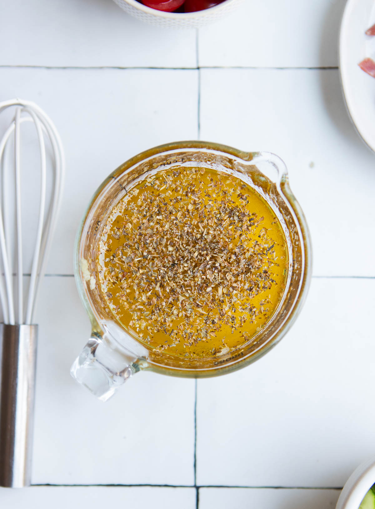 olive oil and lemon juice mixed with herbs in a glass measuring cup to make a salad dressing recipe for pasta salad 
