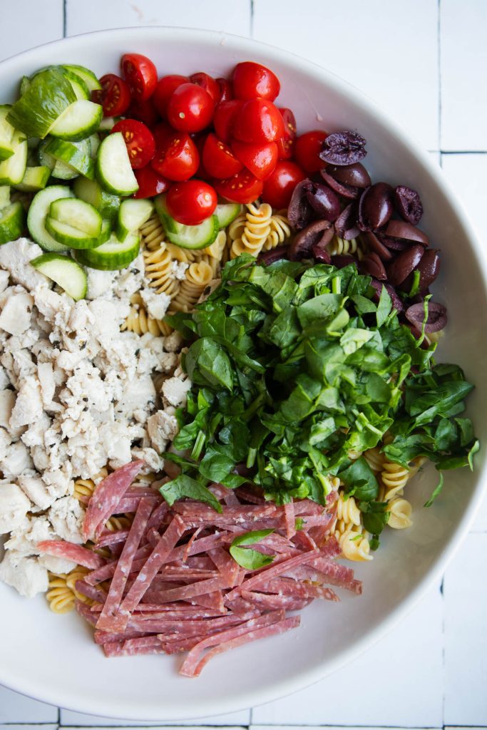 cucumbers, tomatoes, olives, spinach, chicken and salami in a big bowl with protein pasta 