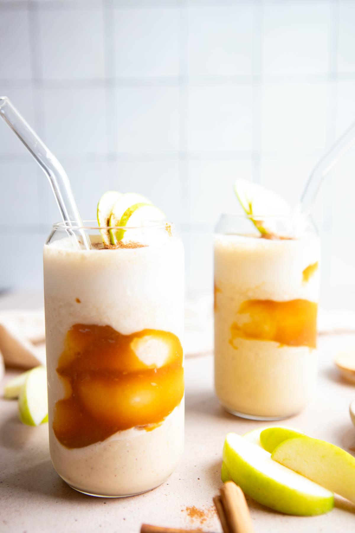 2 tall glasses filled with a cinnamon apple smoothie and topped with apple slices