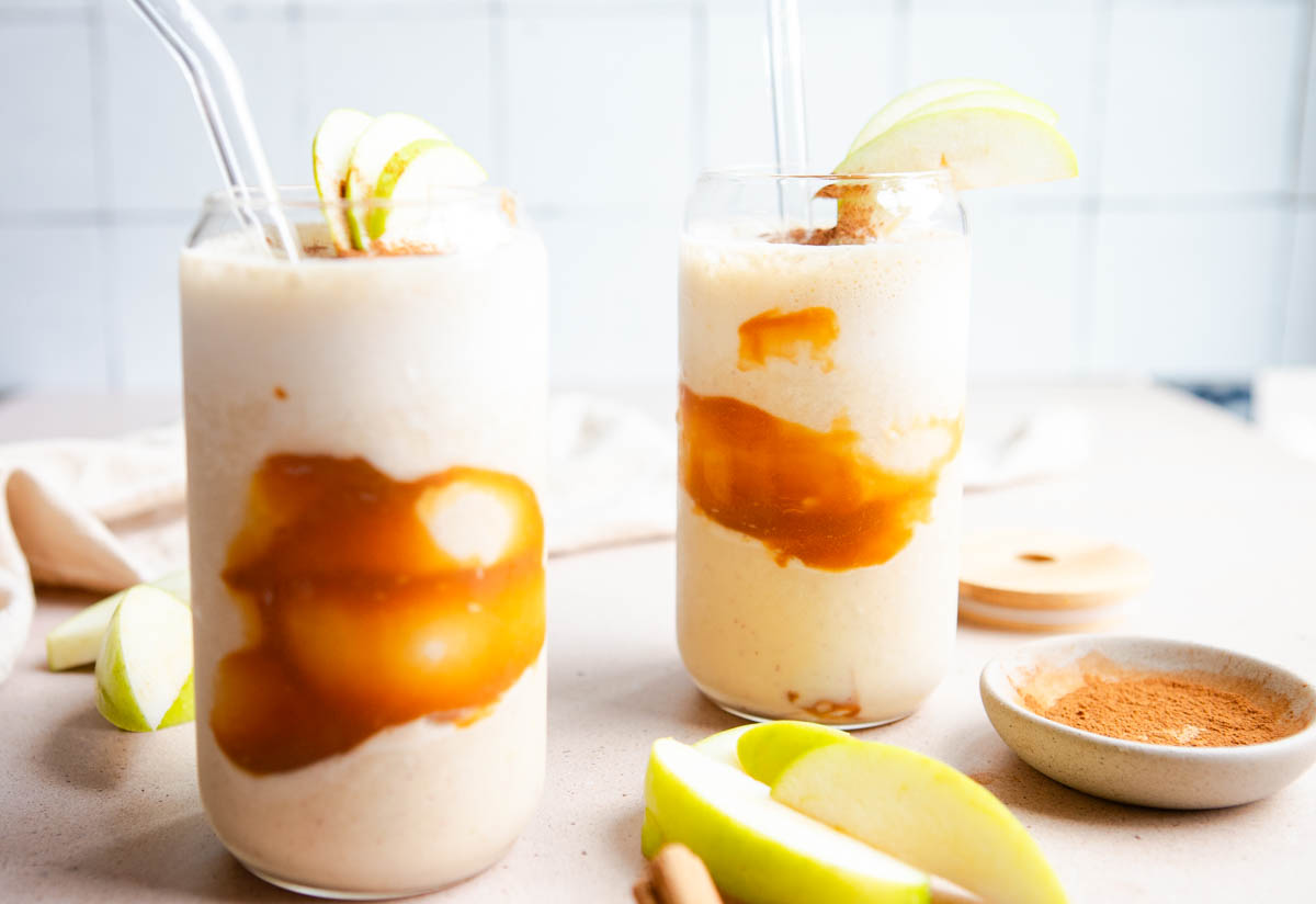 2 glasses filled with apple smoothie and garnished with a caramel swirl and apple slices