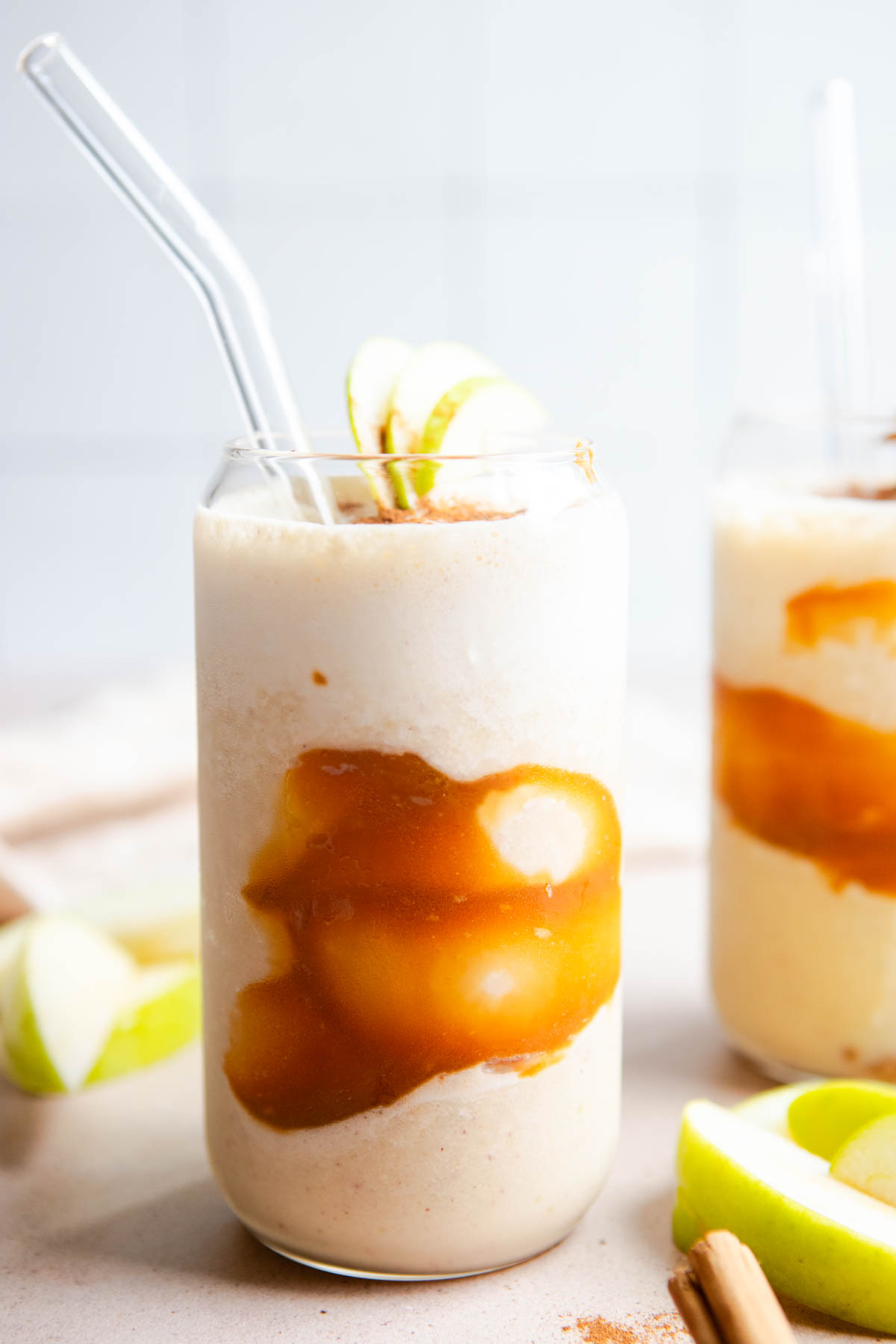 a tall glass with a swirl of caramel sauce and then filled with a apple smoothie and garnished with cinnamon and apples 
