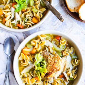 2 bowls filled with homestyle chicken noodle soup and pieces of bread on the side