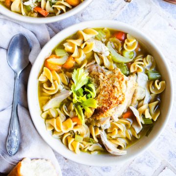 a bowl of warm chicken noodle soup garnished with celery leaves