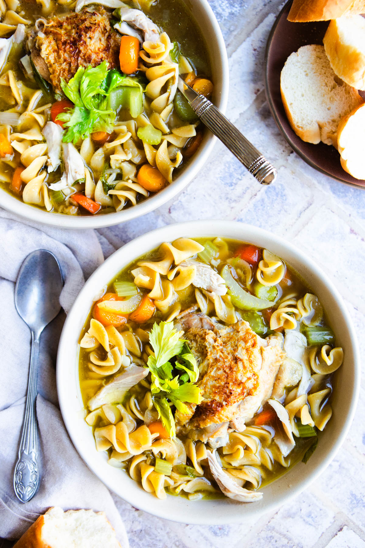 2 bowls filled with homestyle chicken noodle soup and pieces of bread on the side