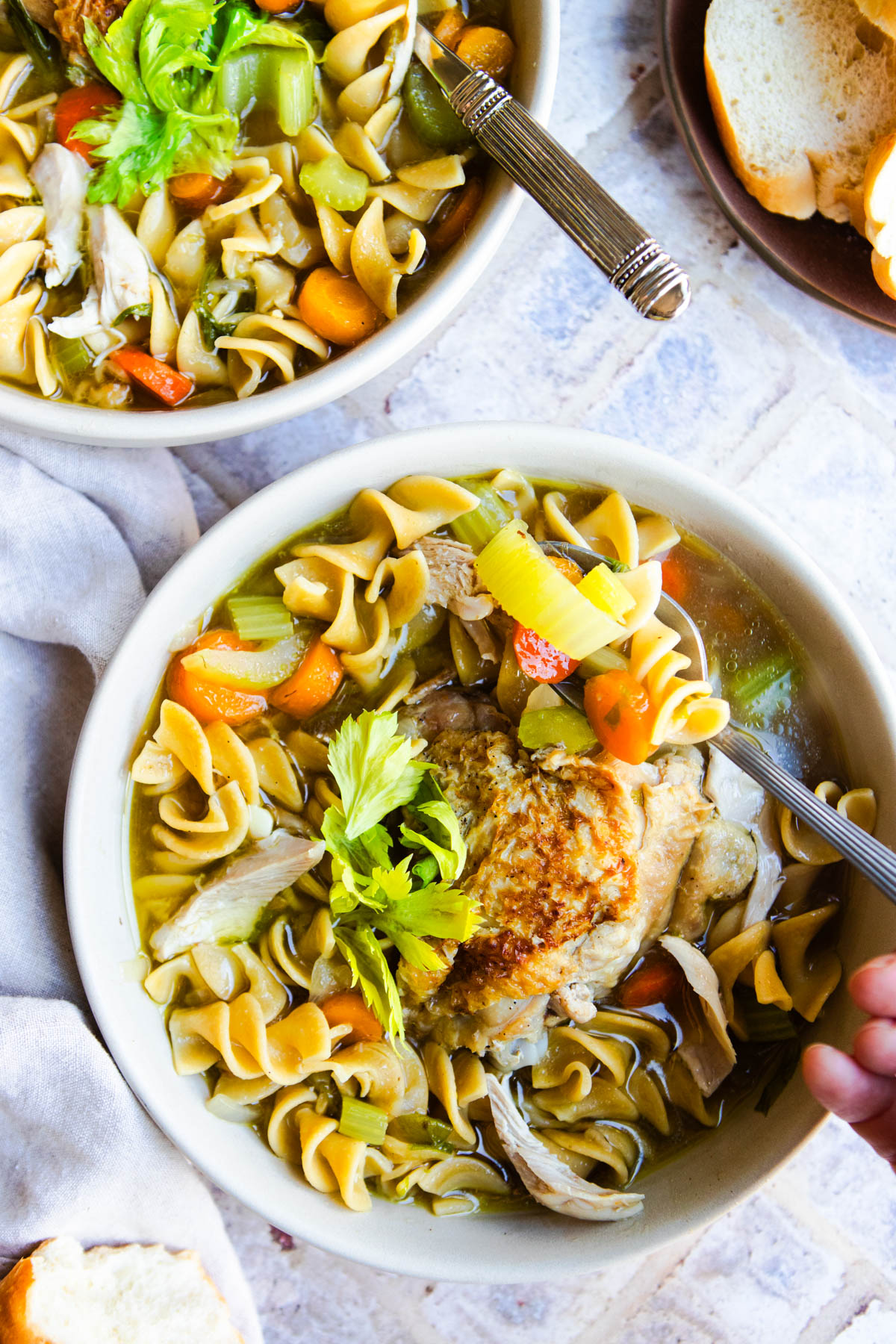 a hand scooping up a spoonful of chicken noodle soup from a white bowl