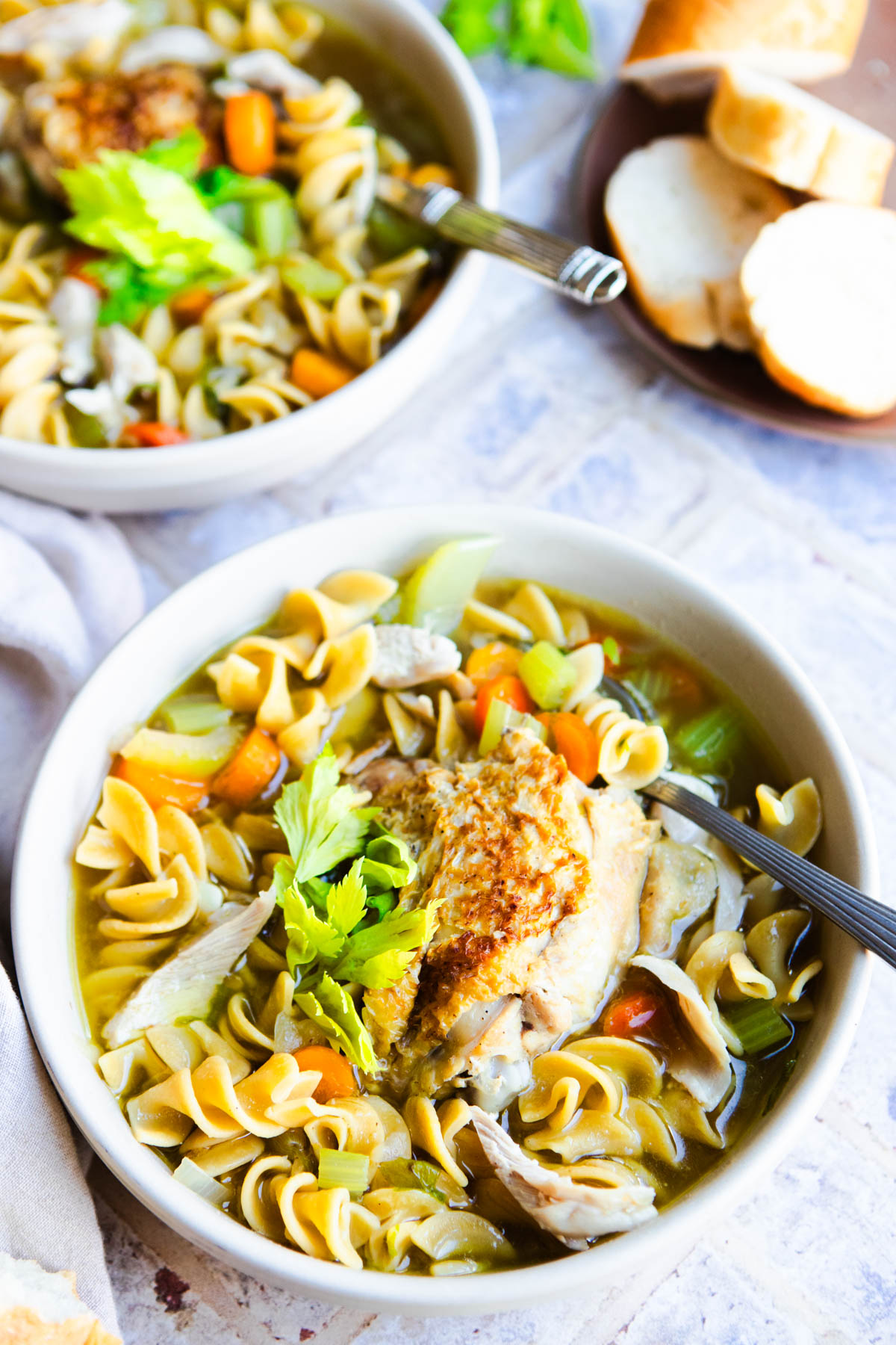 a chicken thigh served in a bowl of chicken noodle soup and garnished with celery leaves