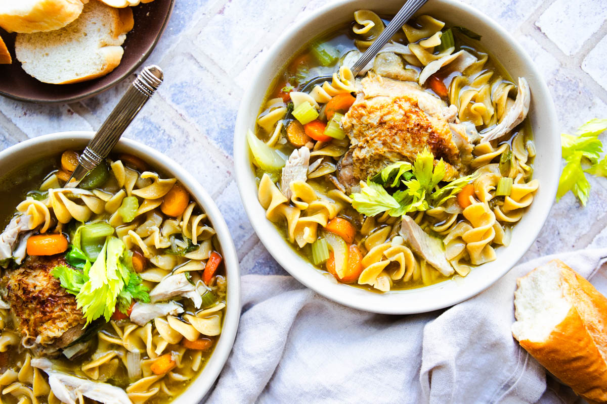 2 bowls filled with homemade chicken noodle soup and garnished with celery leaves