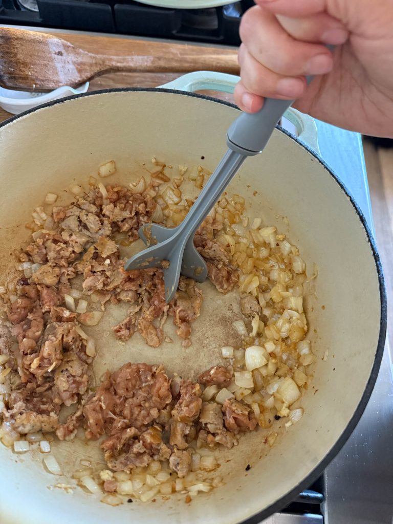 Italian sausage, onion and garlic cooking in a 6 quart Dutch oven
