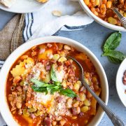 pasta fagioli with sausage in a large white soup bowl and garnished with parmesan cheese and basil leaves