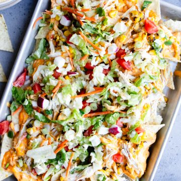 sheet pan filled with chicken nachos topped with veggies for a healthy version
