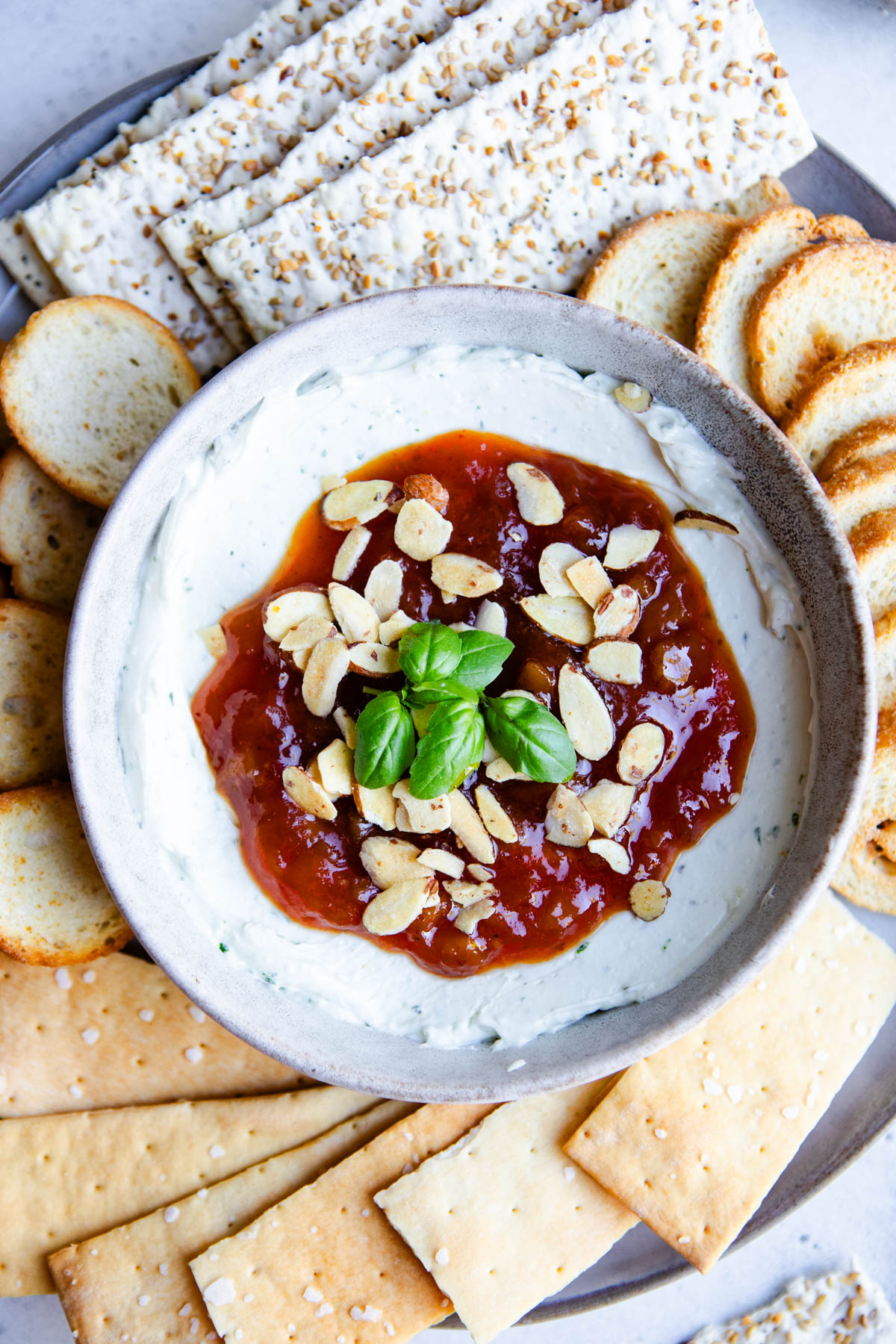 goat cheese dip with mango chutney topping in a bowl set on a plate filled with crackers