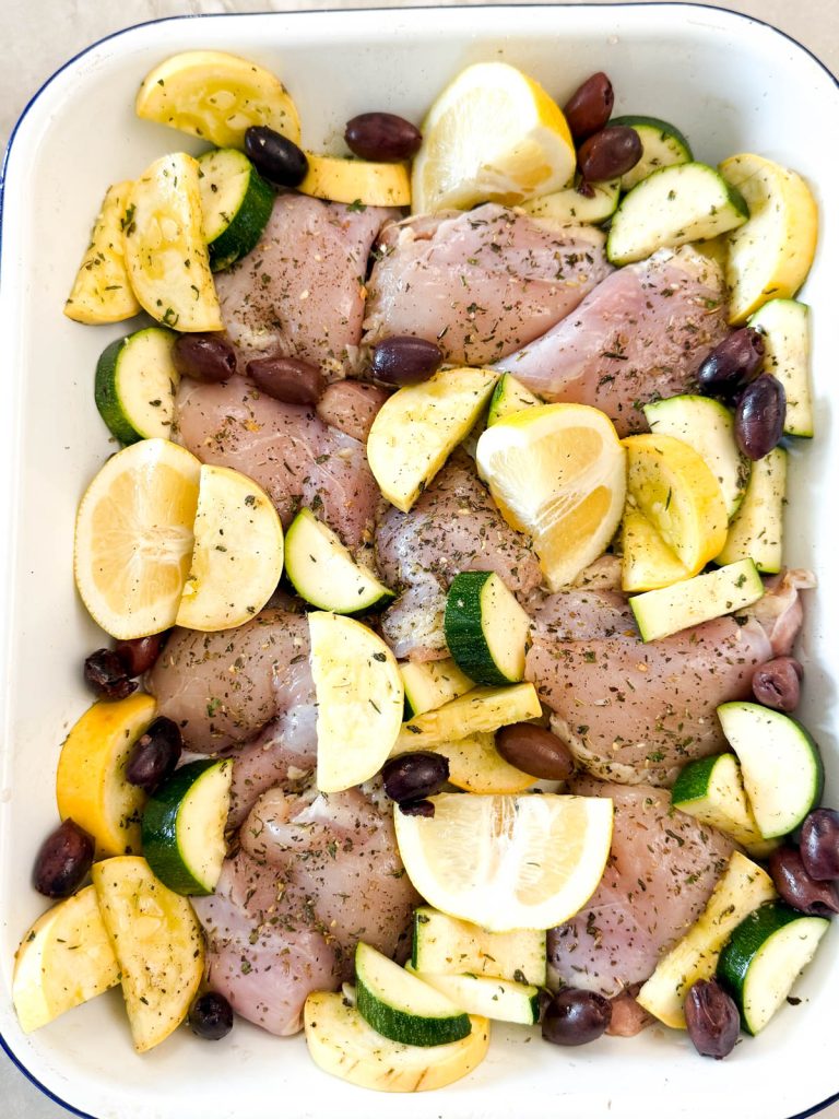 raw chicken thighs and uncooked squash in a baking pan ready to be cooked