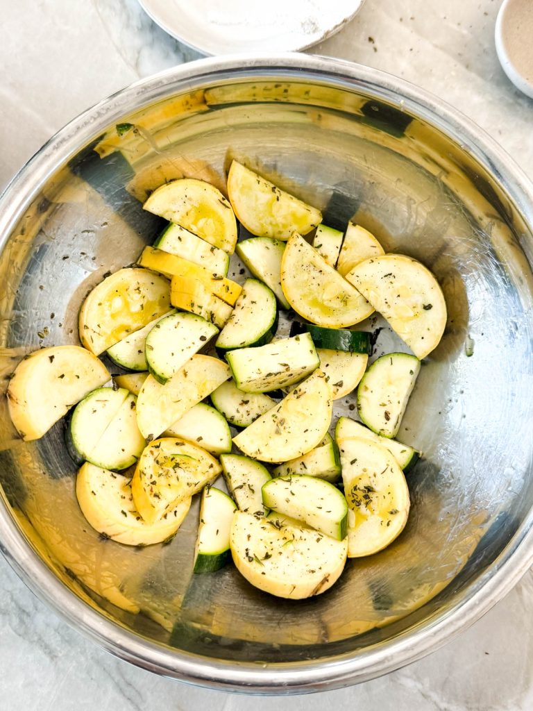 raw uncooked veggies in a mixing bowl tossed with olive oil and Greek seasoning