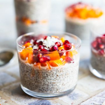 4 glass cups filled with chia seed pudding and garnished with pomegranate and persimmons