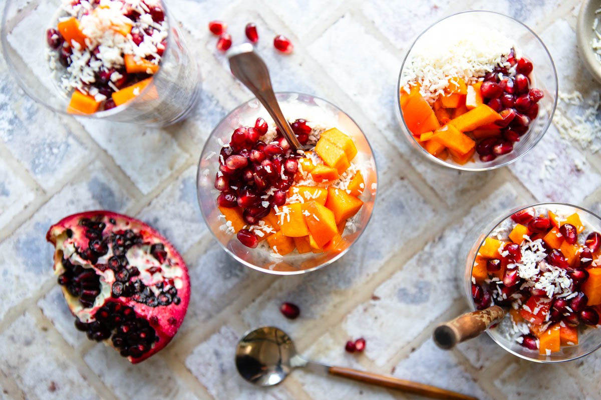 healthy chia seed pudding made with coconut milk and fresh ginger, garnished with persimmons and pomegranates