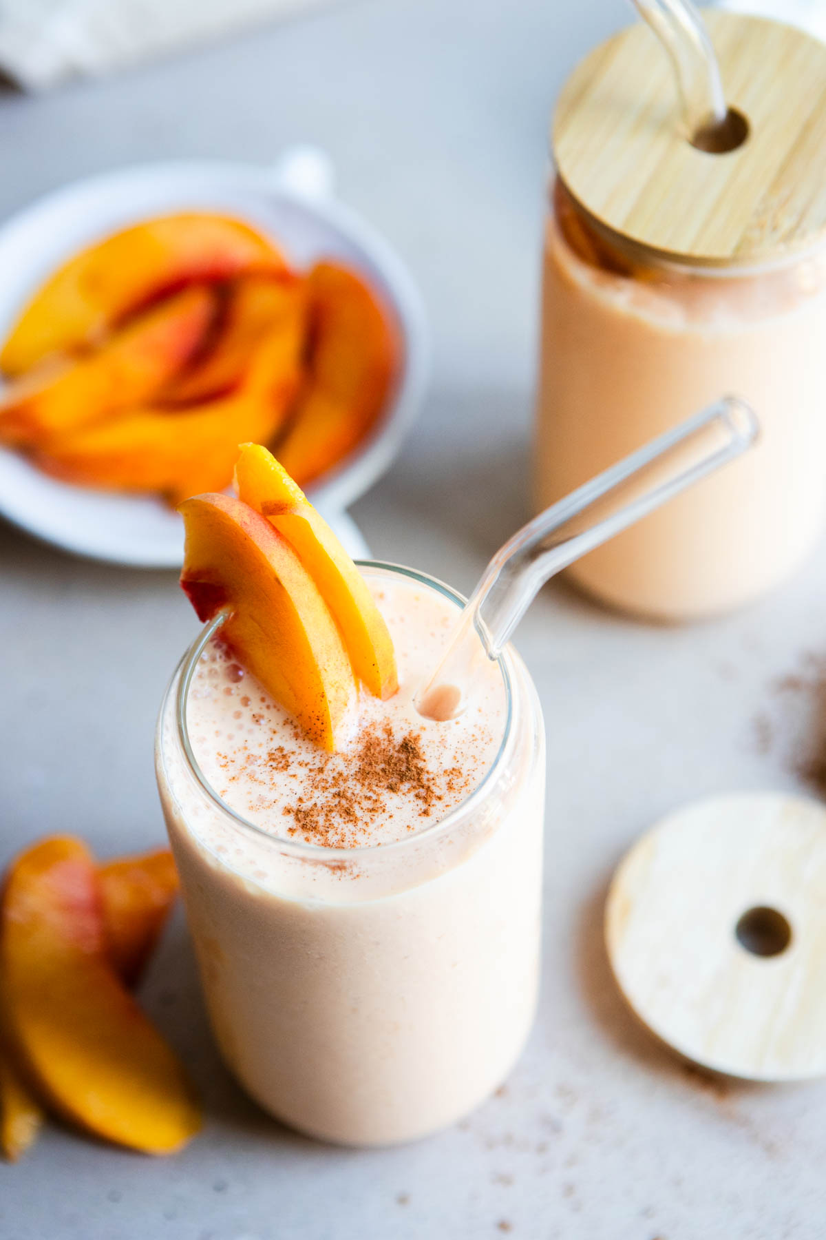 2 tall glasses with bamboo lids filled with cottage cheese smoothie with peaches
