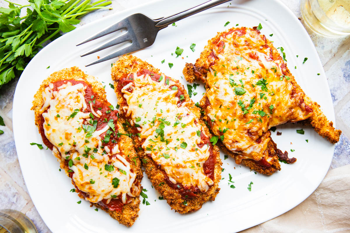 3 pieces of air fried chicken parmesan on a white ceramic platter and sprinkled with diced parsley