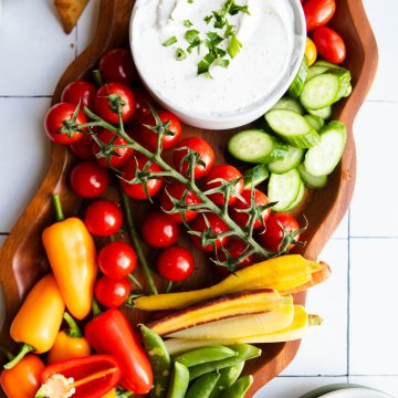 cottage cheese ranch dip in a white bowl set on a wood curvy platter filled with fresh veggies