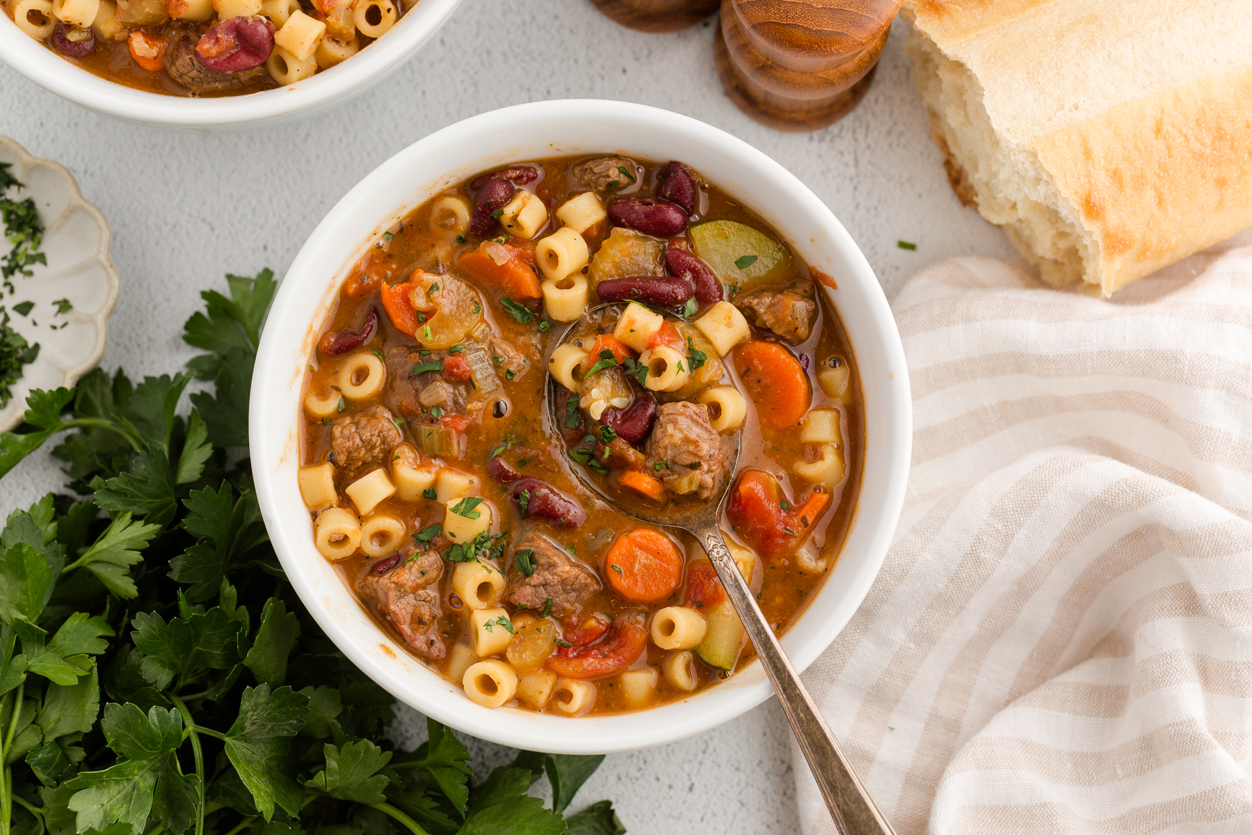 white ceramic bowl filled with beef minestrone soup and served next to crusty bread