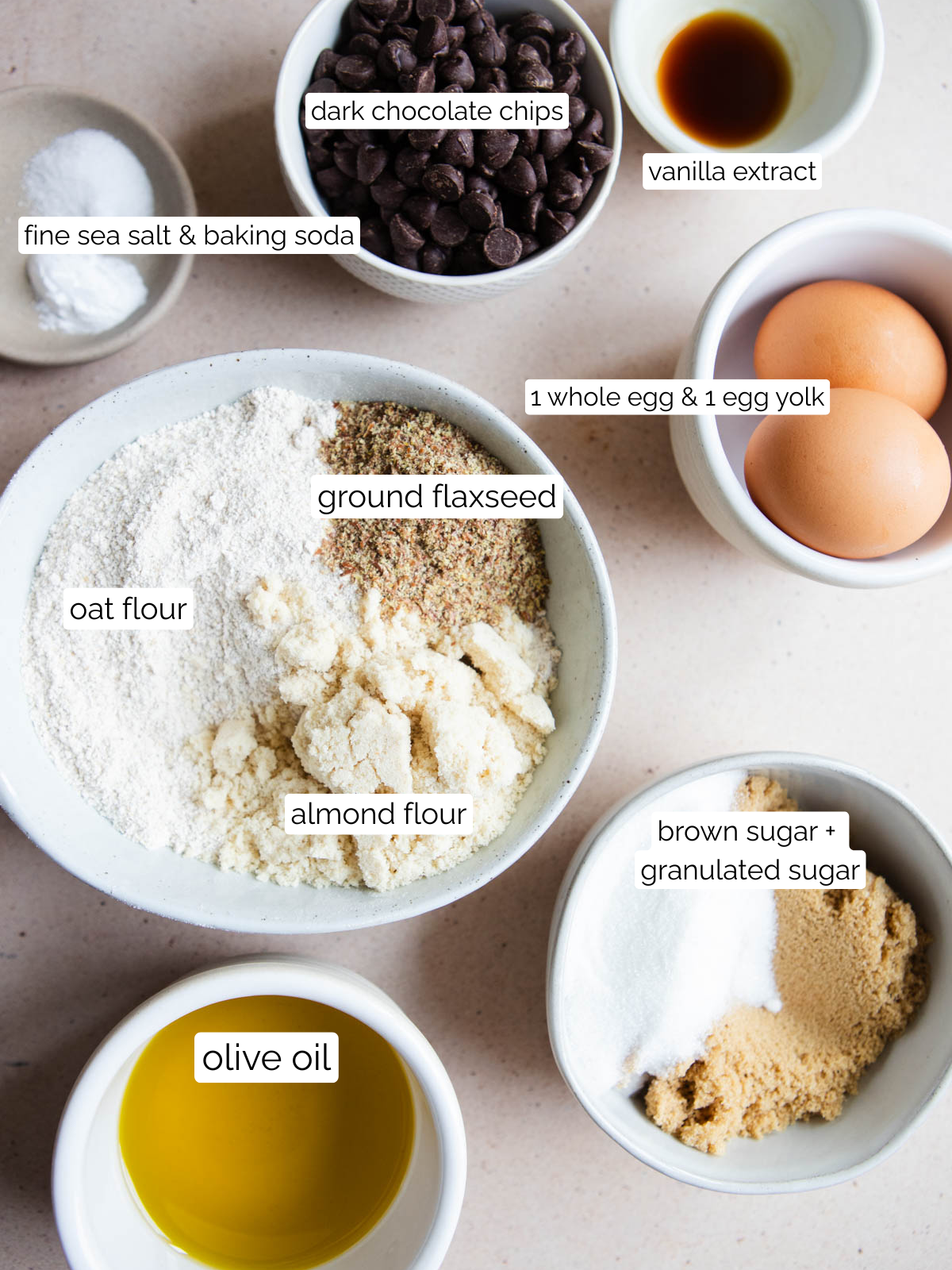 all the ingredients to make chocolate chip cookies using oat flour and olive oil, placed in small white bowls