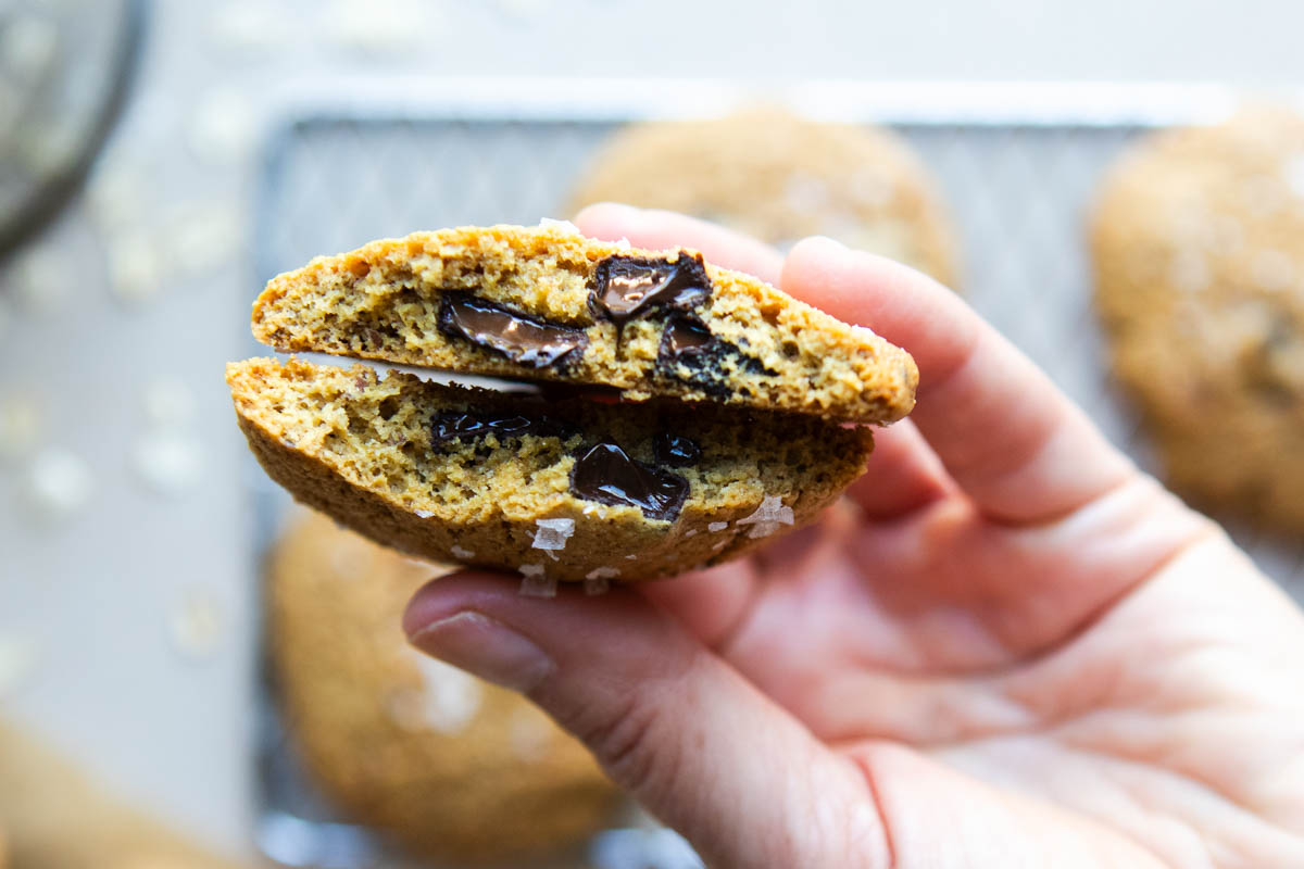 thick chocolate chip cookies made with oat flour and olive oil broken in half to show the texture and gooey center of the cookie