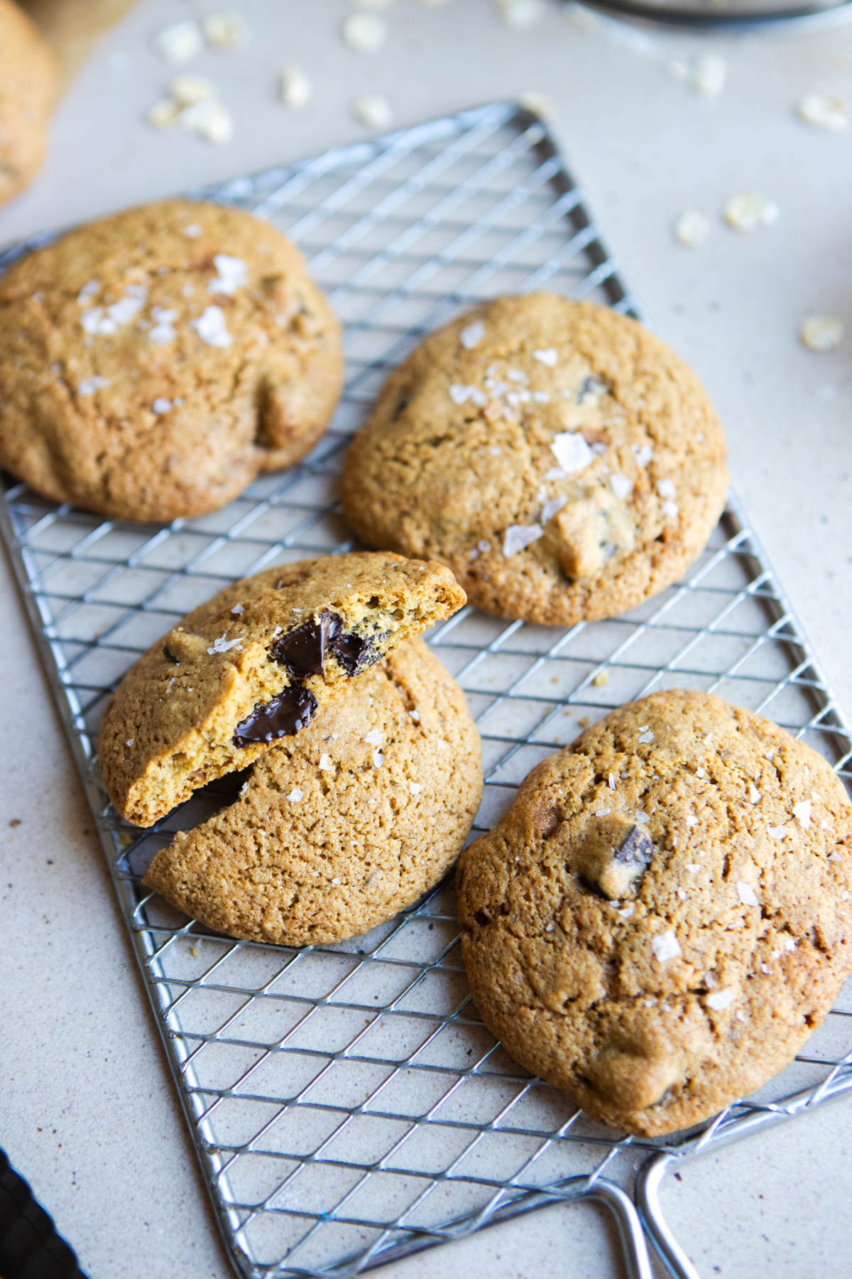 a silver cooling tray topped with chocolate chip cookies fresh out of the oven and sprinkled with flaky salt