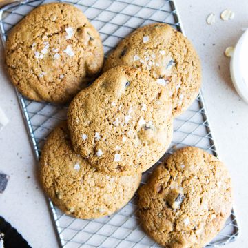 a pile of gooey chocolate chip cookies sprinkled with flaky salt, set on a small cooling tray