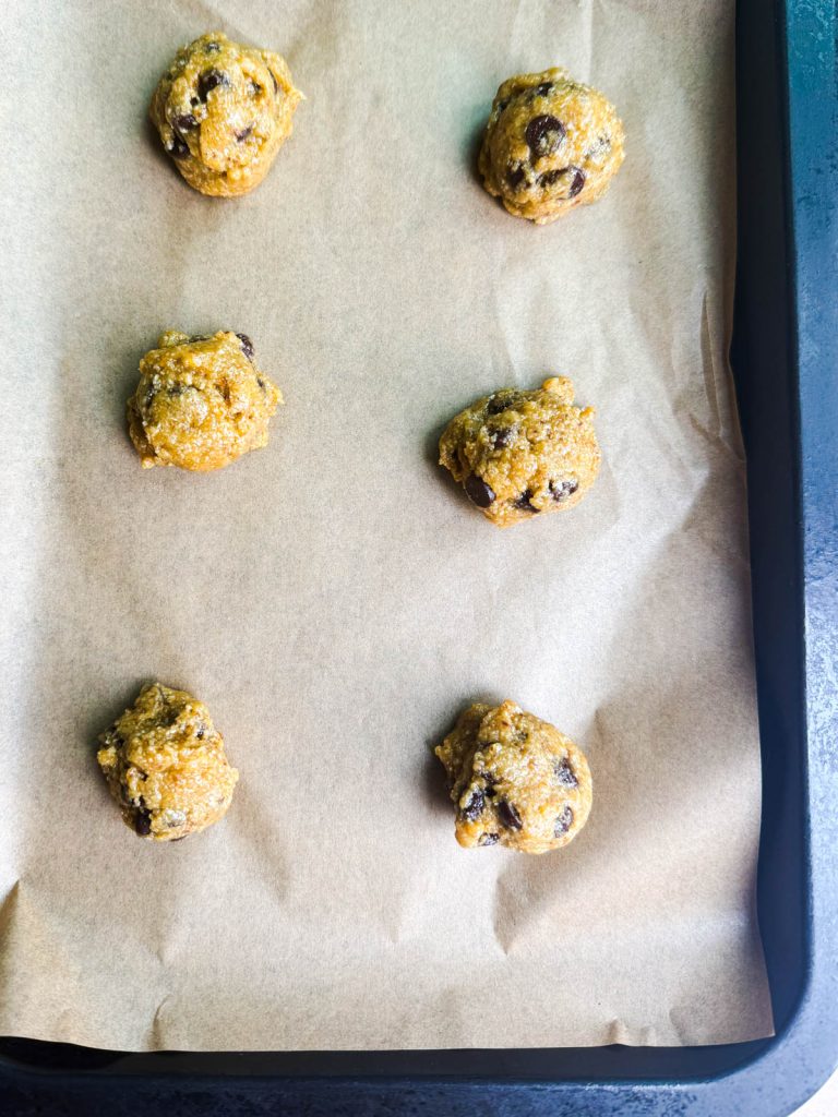 formed mounds of chocolate chip cookie dough on a parchment lined baking tray