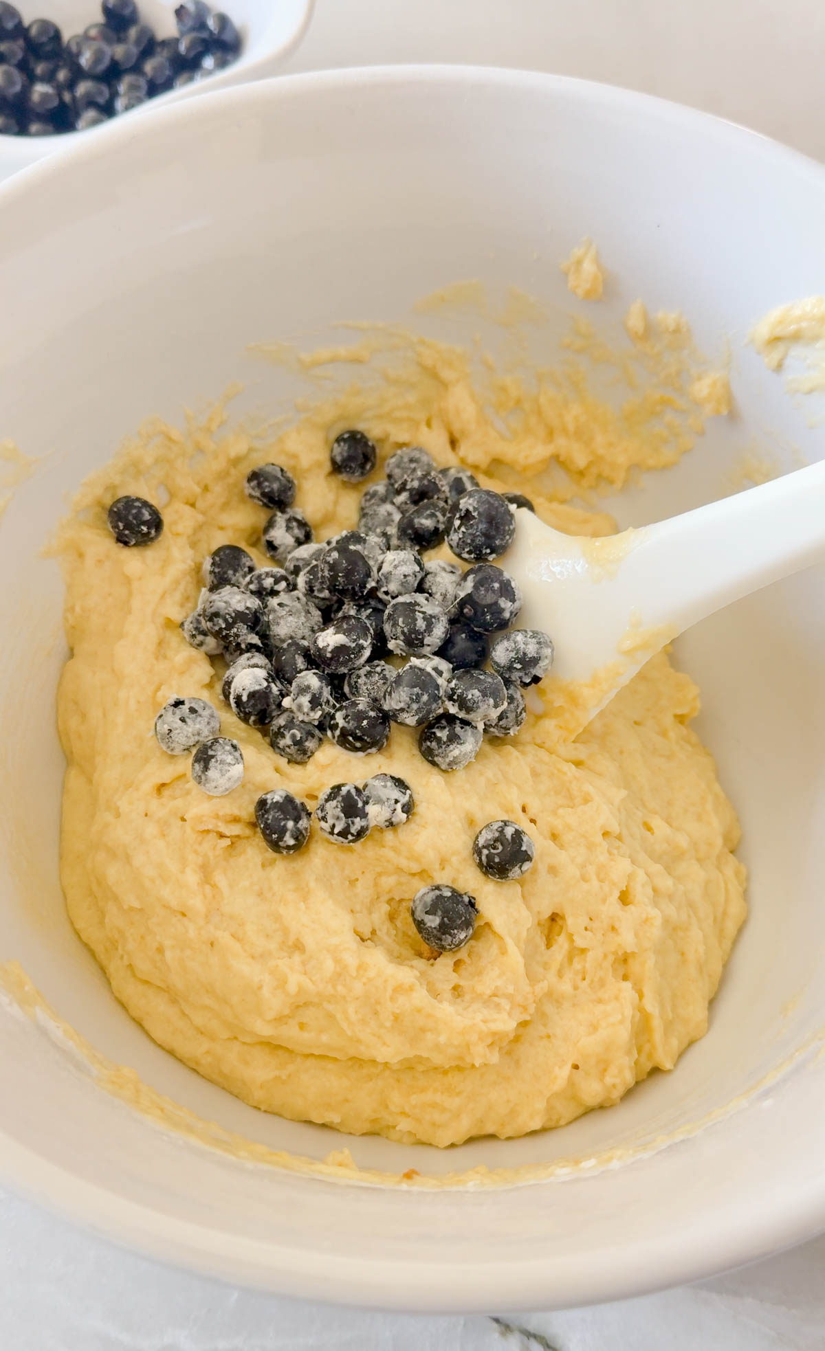 blueberries folded into muffin mix in a white ceramic bowl