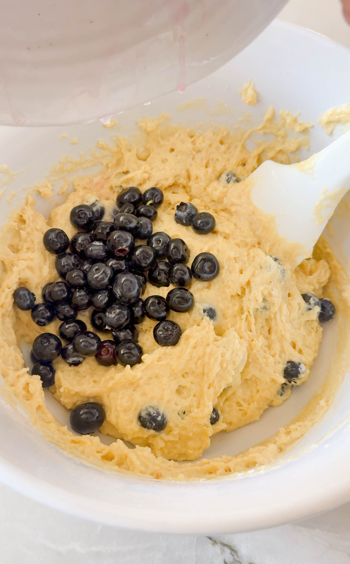 macerated blueberries folded into muffin batter in a mixing bowl