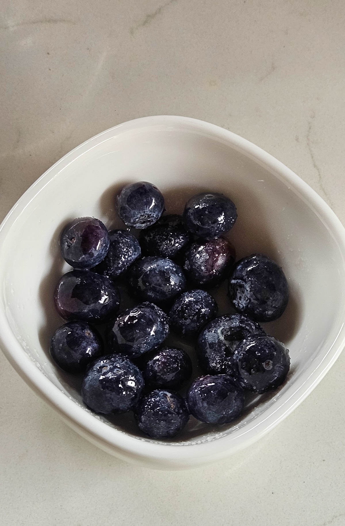 macerated blueberries in a white bowl with lemon juice and sugar
