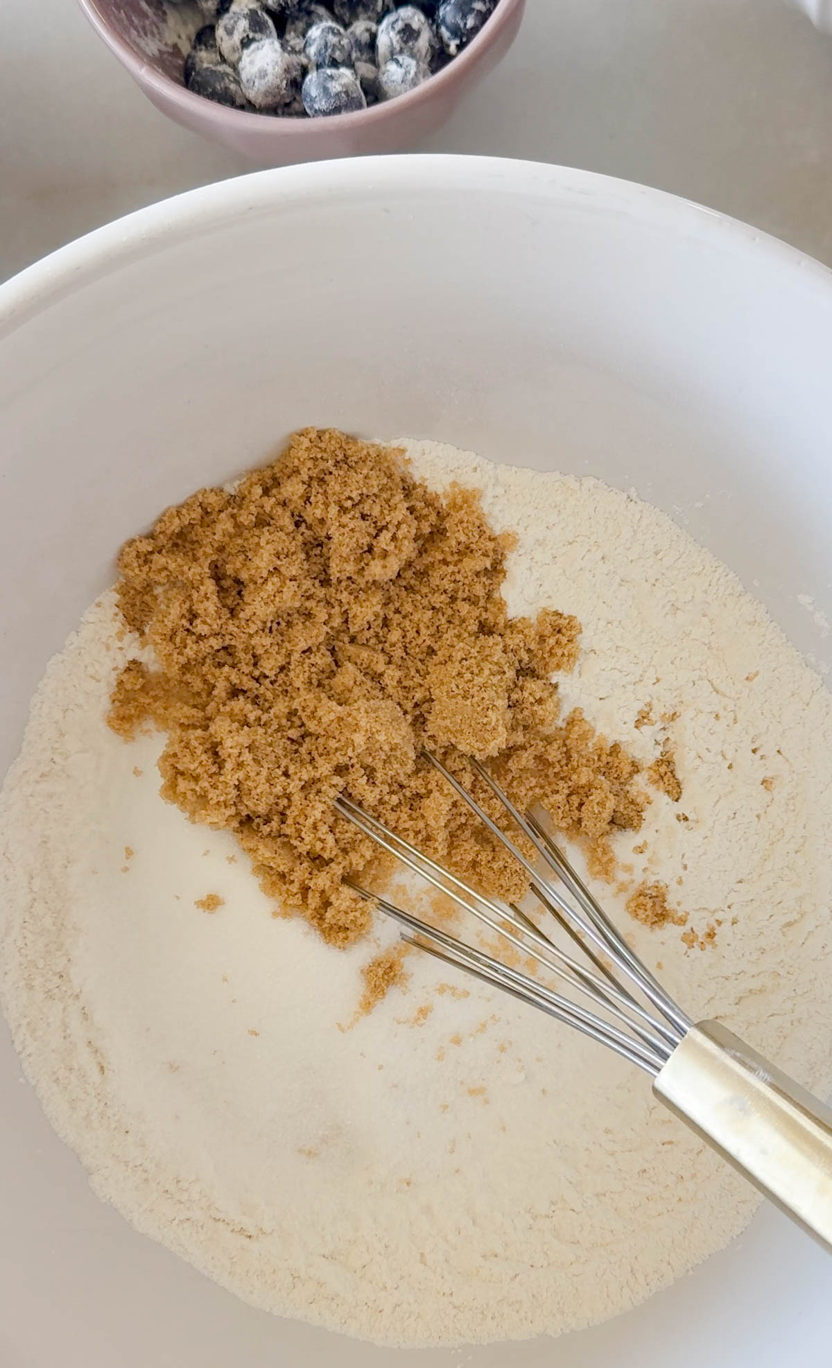 flour, white granulated sugar and brown sugar in a white bowl with a metal whisk