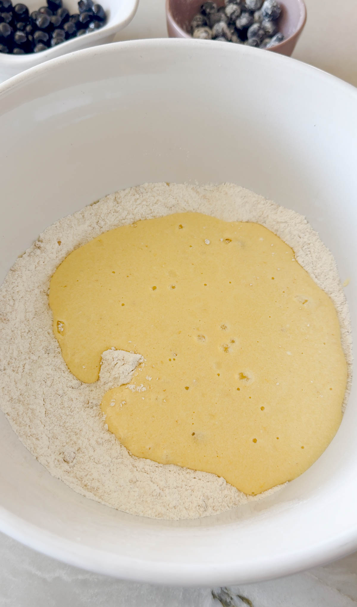 wet and dry ingredients mixed together in a white ceramic mixing bowl to make blueberry muffins