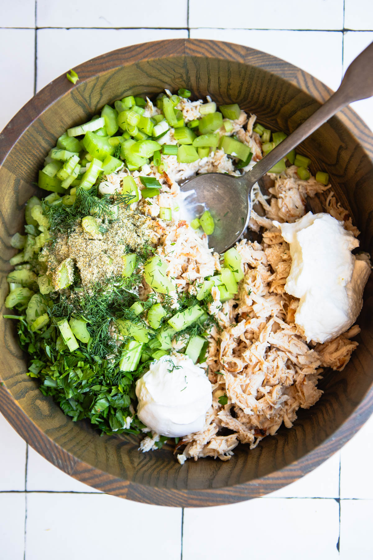 ingredients added to a wood bowl to make healthy chicken salad 